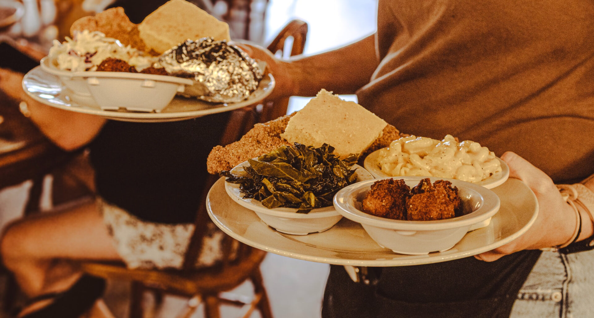 Two plates of Southern food being carried through the dining room at Brown Chicken Brown Cow